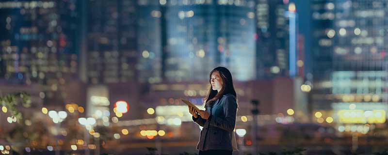 Young businesswoman using digital tablet in financial district, against illuminated corporate skyscrapers at night